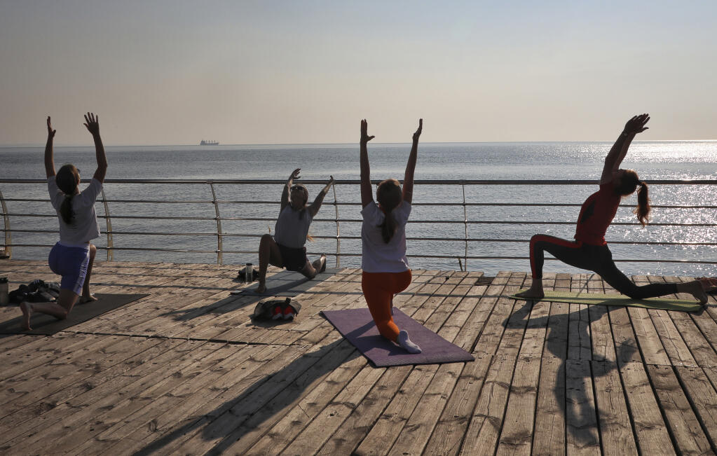 Women practice yoga on a beach by the Black Sea as the ship Navi-Star carrying a load of corn, leaves the port in Odesa, Ukraine, Friday, Aug. 5, 2022. Ukraine is a major global grain supplier but the war had blocked most exports, so the July 22 deal aimed to ease food security around the globe. World food prices have been soaring in a crisis blamed on the war, supply chain problems and COVID-19. (AP Photo/Nina Lyashonok)