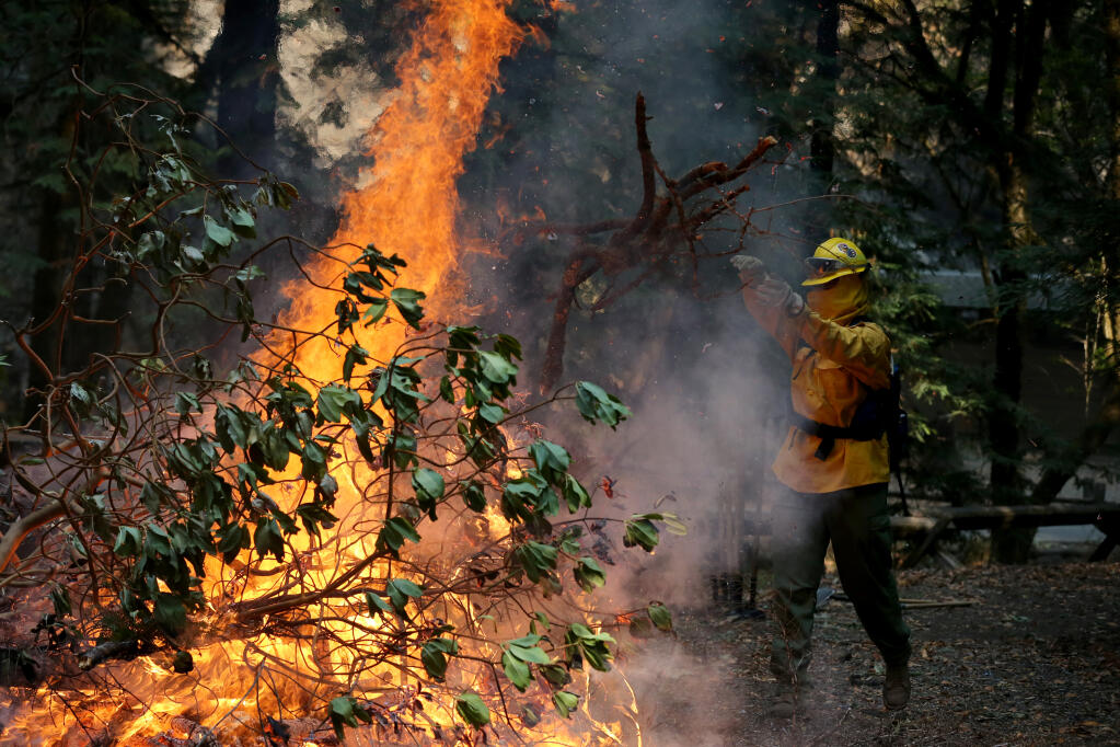 A National Guard member throws a branch on a bonfire as crews work to break down and burn fallen trees and debris at  Armstrong Redwoods State Natural Reserve in Guerneville, Calif., on Monday, Aug. 31, 2020. (BETH SCHLANKER/ The Press Democrat)