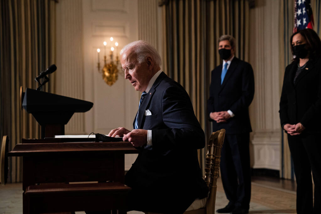 President Joe Biden signs an executive order regarding his administration's response to climate change, in the State Dining Room of the White House in Washington, Wednesday, Jan. 27, 2021. John Kerry, the global envoy for climate change, and Vice President Kamala Harris look on. (Anna Moneymaker/The New York Times)