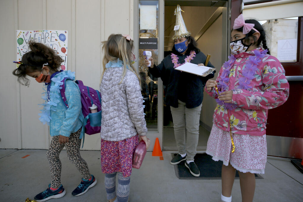 Teaching assistant Yolanda Rodriguez greets first graders Esme Davila, 7, left, Juliette Peterson, 7, and Silvana Rodriguez, 7, right, and takes their temperatures on the first day of in-person learning Sonoma Charter School in Sonoma, California, on Monday, March 1, 2021. (Beth Schlanker/ The Press Democrat)
