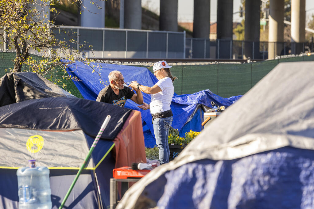 Volunteer Sherrie Vaughn helps a homeless person wake up with a drink of water in the Park & Ride homeless tent encampment near Roberts Lake in northern Rohnert Park on Monday, Feb. 7, 2022. (Photo by John Burgess/The Press Democrat)
