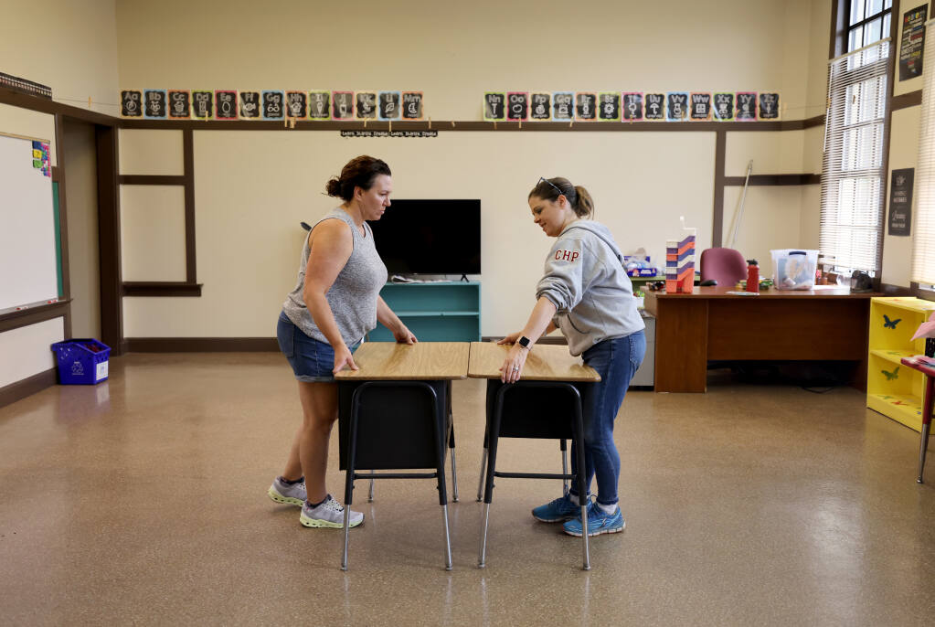 Art teacher Aimee Reed-Heidenreich, left, and sixth grade teacher Brenna Pourroy move desks into a classroom at the new Mayacamas Charter Middle School, formerly St. John the Baptist Catholic School, in Napa, Tuesday, Aug. 8, 2023. (Beth Schlanker / The Press Democrat)