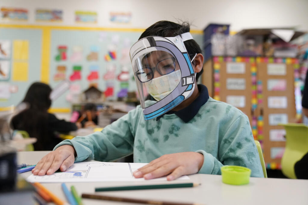 A student wears a mask and face shield in a 4th grade class amid the COVID-19 pandemic at Washington Elementary School Wednesday, Jan. 12, 2022, in Lynwood, Calif.   (AP Photo/Marcio Jose Sanchez)