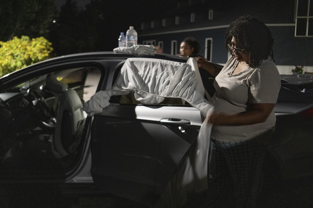 Chrystal Audet and her daughter, Cierra, place sheets on the windows of their car to create privacy, in Kirkland, Wash. on Aug. 27, 2023. The family is among a growing cohort of working Americans living out of their cars. (Ruth Fremson/The New York Times)